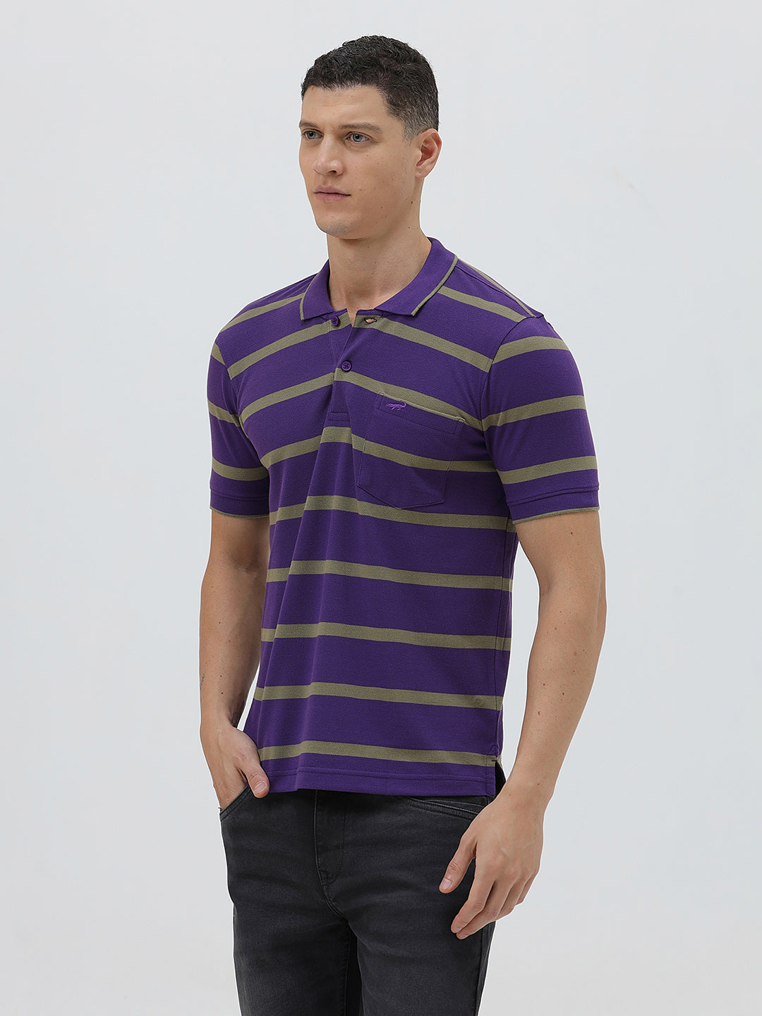 A man wearing a purple short-sleeve polo shirt with horizontal olive green stripes, paired with dark gray pants, standing against a light gray studio background.