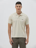 A man wearing a light beige short-sleeve polo shirt with subtle horizontal stripe details and a small crocodile logo on the left chest, paired with olive green trousers, against a plain light gray background.