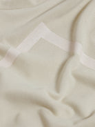A man wearing a light beige short-sleeve polo shirt with subtle horizontal stripe details and a small crocodile logo on the left chest, paired with olive green trousers, against a plain light gray background.