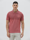 A man wearing a heathered dusty rose pink polo shirt with a tonal embroidered crest on the left chest, paired with light beige trousers, against a plain light gray background.
