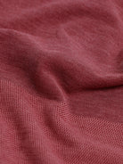A man wearing a heathered dusty rose pink polo shirt with a tonal embroidered crest on the left chest, paired with light beige trousers, against a plain light gray background.