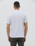 A man wearing a white short-sleeve polo shirt with a gray geometric pattern, paired with dark gray trousers, standing against a light gray studio background.