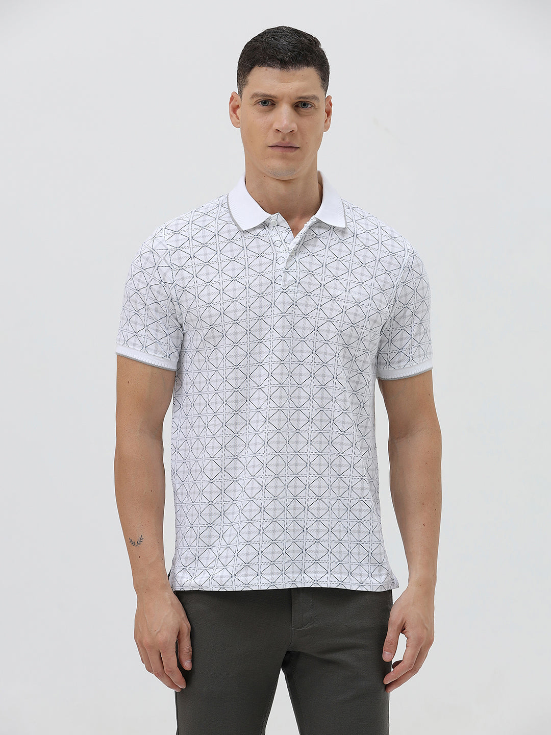 A man wearing a white short-sleeve polo shirt with a gray geometric pattern, paired with dark gray trousers, standing against a light gray studio background.