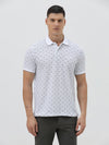 A man wearing a white short-sleeve polo shirt with a gray geometric pattern, paired with dark gray trousers, standing against a light gray studio background.