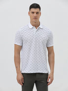 A man wearing a white short-sleeve polo shirt with a gray geometric pattern, paired with dark gray trousers, standing against a light gray studio background.