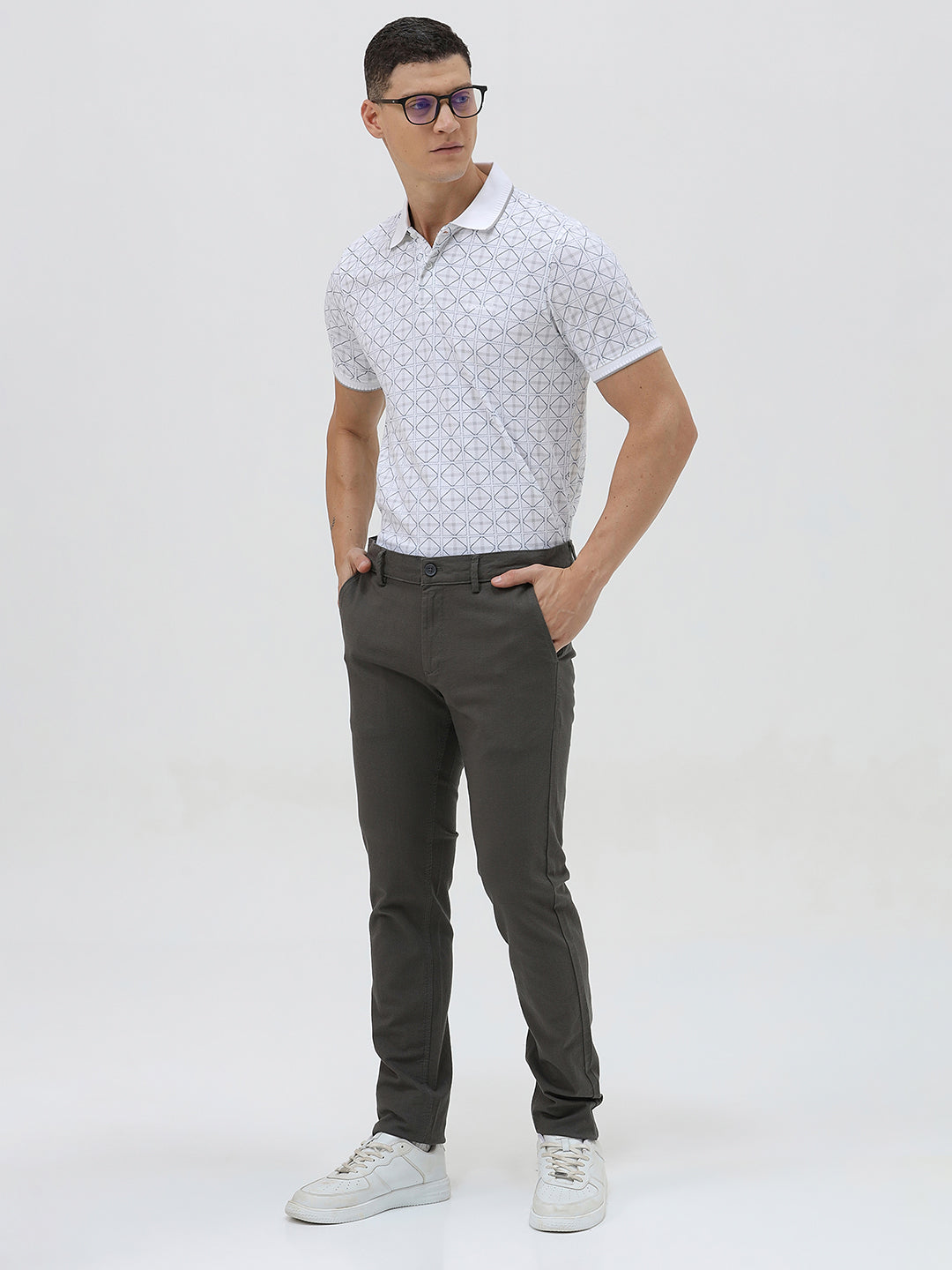 A man wearing a white short-sleeve polo shirt with a gray geometric pattern, paired with dark gray trousers, standing against a light gray studio background.