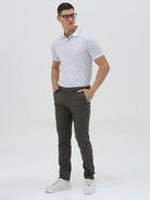 A man wearing a white short-sleeve polo shirt with a gray geometric pattern, paired with dark gray trousers, standing against a light gray studio background.
