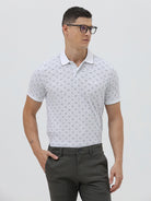 A man wearing a white short-sleeve polo shirt with a gray geometric pattern, paired with dark gray trousers, standing against a light gray studio background.