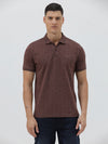 A man wearing a short-sleeve polo shirt in a dark brownish-rose color with a subtle tonal geometric pattern, paired with dark jeans, against a light gray studio background.