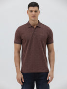 A man wearing a short-sleeve polo shirt in a dark brownish-rose color with a subtle tonal geometric pattern, paired with dark jeans, against a light gray studio background.