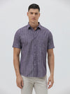 A man wearing a short-sleeve button-up shirt with a purple and white vertical stripe pattern, paired with light beige trousers, standing against a light gray studio background.