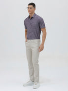 A man wearing a short-sleeve button-up shirt with a purple and white vertical stripe pattern, paired with light beige trousers, standing against a light gray studio background.