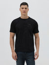 A man wearing a black short-sleeve t-shirt with a subtle tonal geometric pattern and a small 'Gildan' logo on the left chest, paired with dark blue jeans, against a light gray studio background.