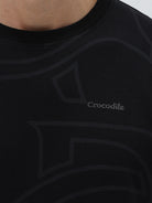 A man wearing a black short-sleeve t-shirt with a subtle tonal geometric pattern and a small 'Gildan' logo on the left chest, paired with dark blue jeans, against a light gray studio background.