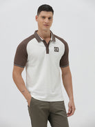 A man wearing a short-sleeve raglan polo shirt with a white body and brown sleeves, featuring a striped collar and a small 'CR' logo patch on the chest, paired with olive green pants against a light gray background.