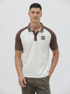 A man wearing a short-sleeve raglan polo shirt with a white body and brown sleeves, featuring a striped collar and a small 'CR' logo patch on the chest, paired with olive green pants against a light gray background.