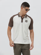 A man wearing a short-sleeve raglan polo shirt with a white body and brown sleeves, featuring a striped collar and a small 'CR' logo patch on the chest, paired with olive green pants against a light gray background.