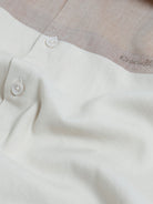 A man wearing a short-sleeve raglan polo shirt with a white body and brown sleeves, featuring a striped collar and a small 'CR' logo patch on the chest, paired with olive green pants against a light gray background.