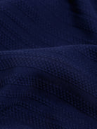 A man wearing a navy blue short-sleeve polo shirt with a small embroidered crocodile logo on the chest, paired with dark gray jeans, against a light gray studio background.