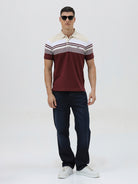 A man wearing a short-sleeve polo shirt with a colorblock design of cream, white, and burgundy, paired with dark blue jeans, against a plain light gray background.