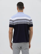 A man wearing a short-sleeve polo shirt with horizontal stripes in light blue, white, and navy, paired with light gray trousers, against a plain light gray background.