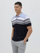 A man wearing a short-sleeve polo shirt with horizontal stripes in light blue, white, and navy, paired with light gray trousers, against a plain light gray background.
