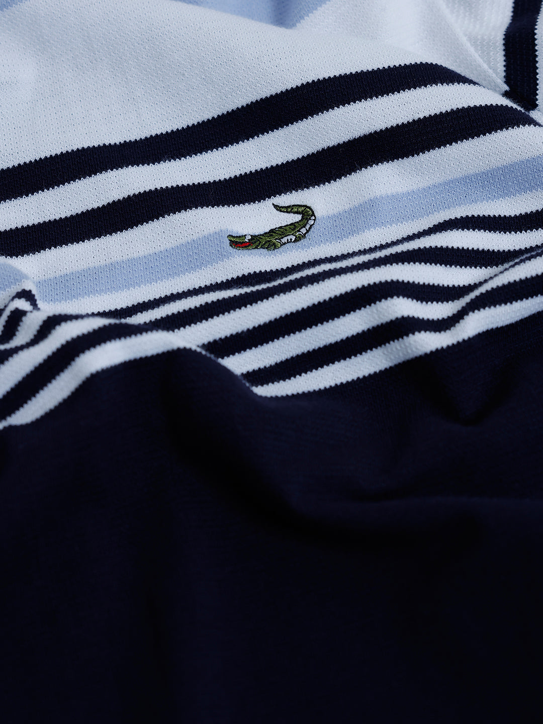 A man wearing a short-sleeve polo shirt with horizontal stripes in light blue, white, and navy, paired with light gray trousers, against a plain light gray background.