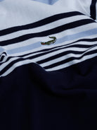 A man wearing a short-sleeve polo shirt with horizontal stripes in light blue, white, and navy, paired with light gray trousers, against a plain light gray background.