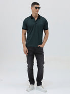 A person wearing slim-fit black denim jeans with a dark green top and white sneakers, shown from the waist down against a plain light gray studio background.