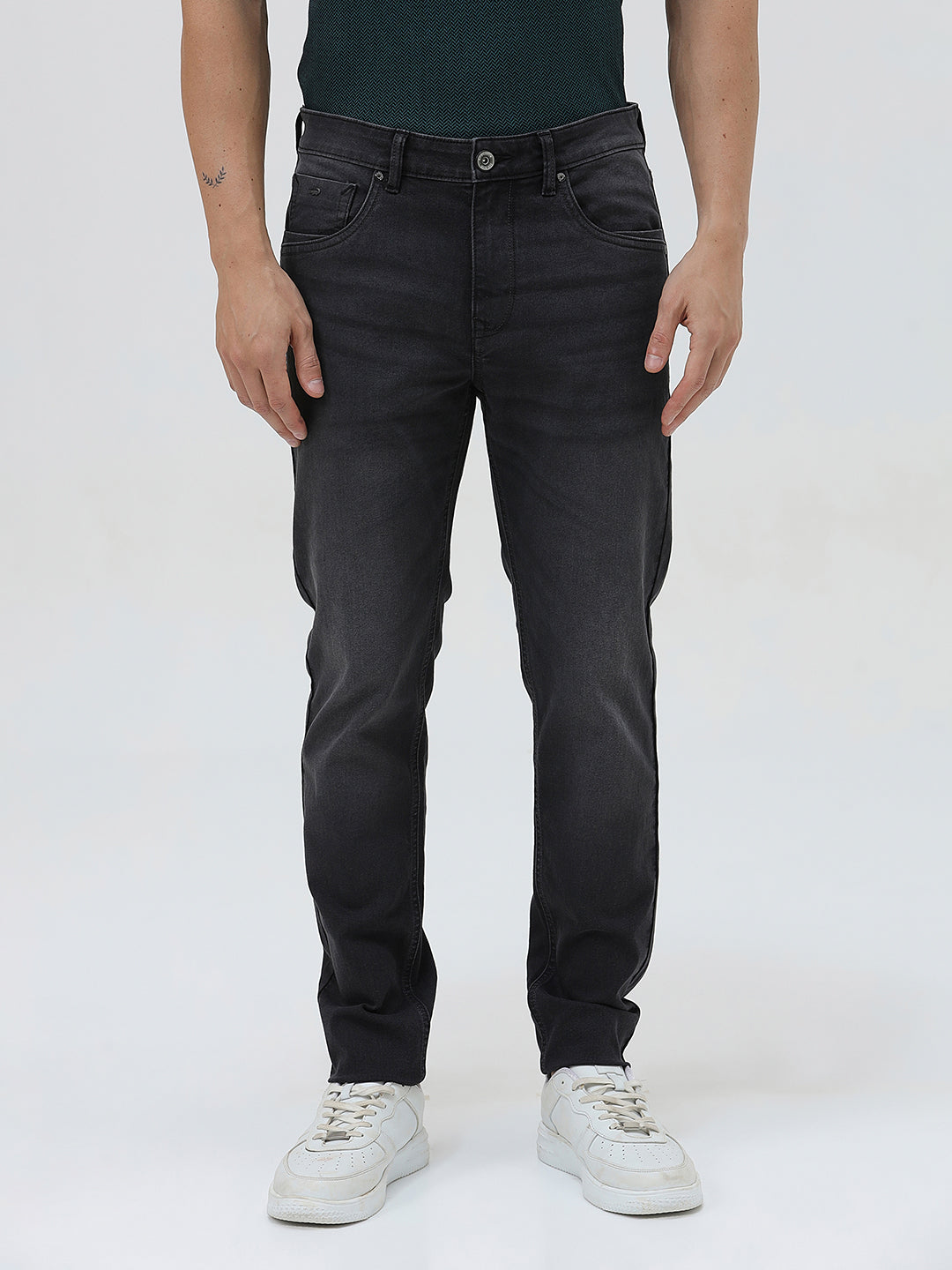 A person wearing slim-fit black denim jeans with a dark green top and white sneakers, shown from the waist down against a plain light gray studio background.