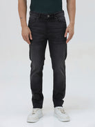 A person wearing slim-fit black denim jeans with a dark green top and white sneakers, shown from the waist down against a plain light gray studio background.