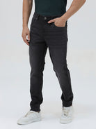 A person wearing slim-fit black denim jeans with a dark green top and white sneakers, shown from the waist down against a plain light gray studio background.
