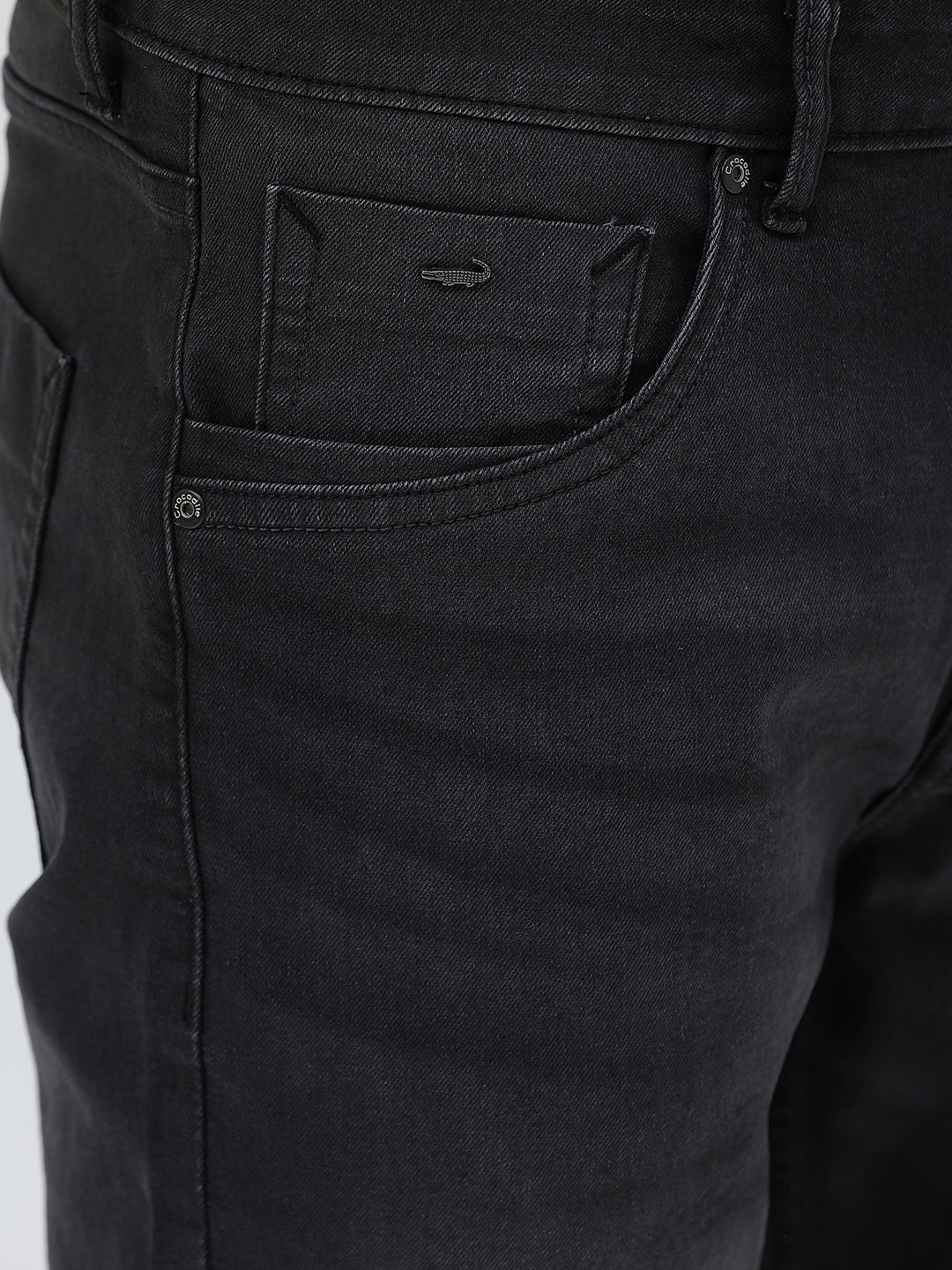 A person wearing slim-fit black denim jeans with a dark green top and white sneakers, shown from the waist down against a plain light gray studio background.