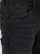 A person wearing slim-fit black denim jeans with a dark green top and white sneakers, shown from the waist down against a plain light gray studio background.