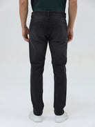 A person wearing slim-fit black denim jeans with a dark green top and white sneakers, shown from the waist down against a plain light gray studio background.