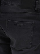 A person wearing slim-fit black denim jeans with a dark green top and white sneakers, shown from the waist down against a plain light gray studio background.