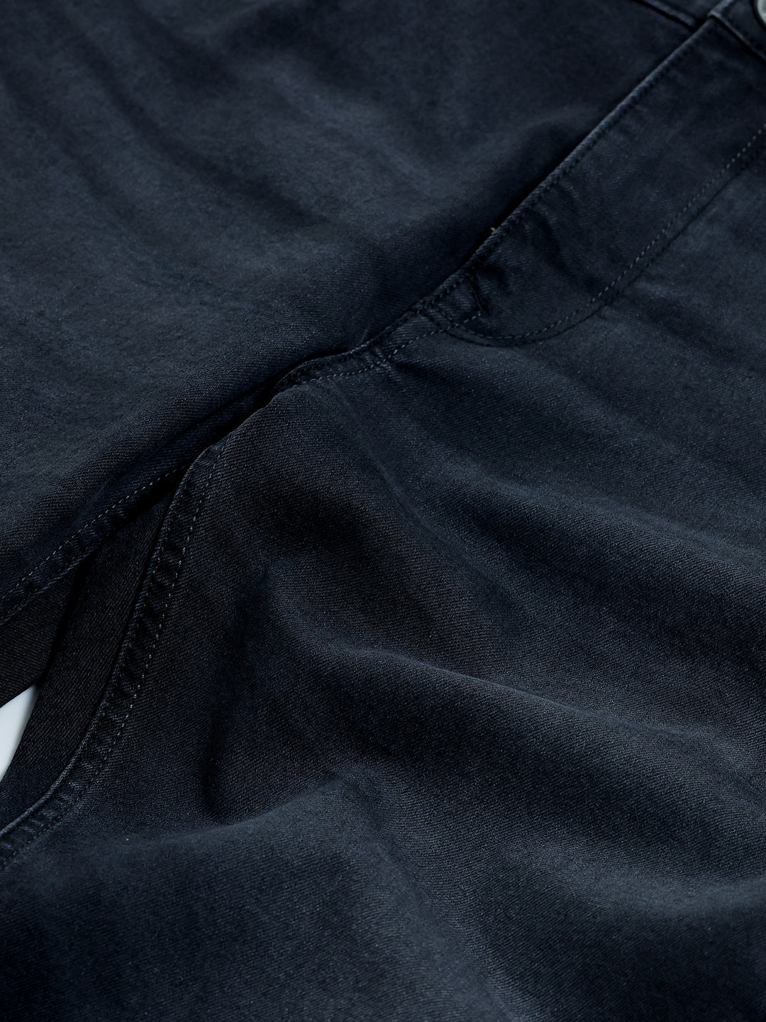 A person wearing slim-fit black denim jeans with a dark green top and white sneakers, shown from the waist down against a plain light gray studio background.