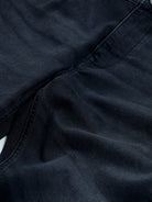 A person wearing slim-fit black denim jeans with a dark green top and white sneakers, shown from the waist down against a plain light gray studio background.