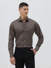 A man wearing a long-sleeve button-down dress shirt in a dark taupe-brown color, paired with black trousers, photographed against a light gray studio background.