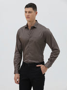 A man wearing a long-sleeve button-down dress shirt in a dark taupe-brown color, paired with black trousers, photographed against a light gray studio background.