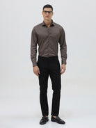 A man wearing a long-sleeve button-down dress shirt in a dark taupe-brown color, paired with black trousers, photographed against a light gray studio background.
