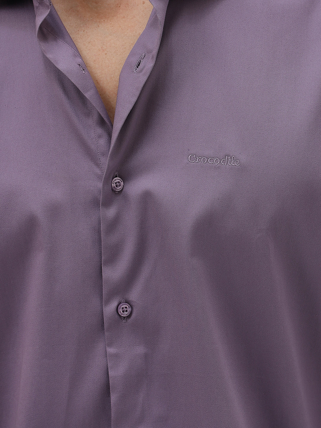A man wearing a long-sleeve button-down shirt in a muted purple shade, paired with dark blue jeans, standing against a light gray studio background.