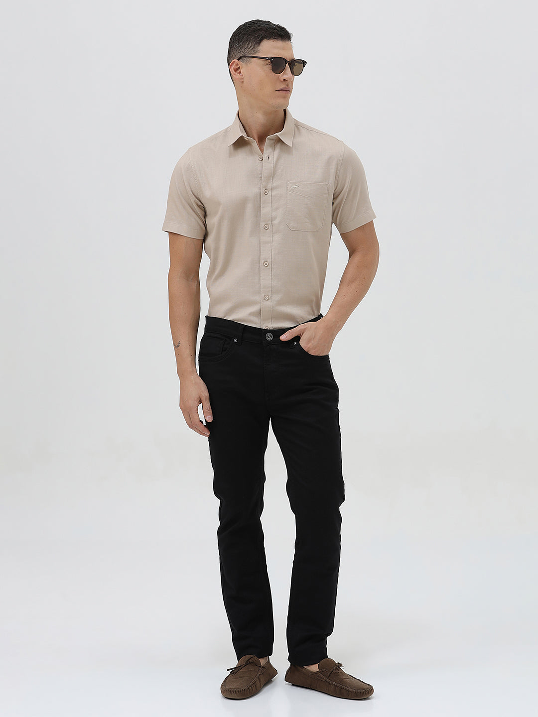 A man wearing a dusty rose long-sleeve button-down shirt and light beige trousers, standing against a light gray studio background.