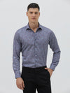 A man wearing a long-sleeve button-up shirt with a subtle blue and purple abstract pattern, paired with black trousers, standing against a light gray studio background.