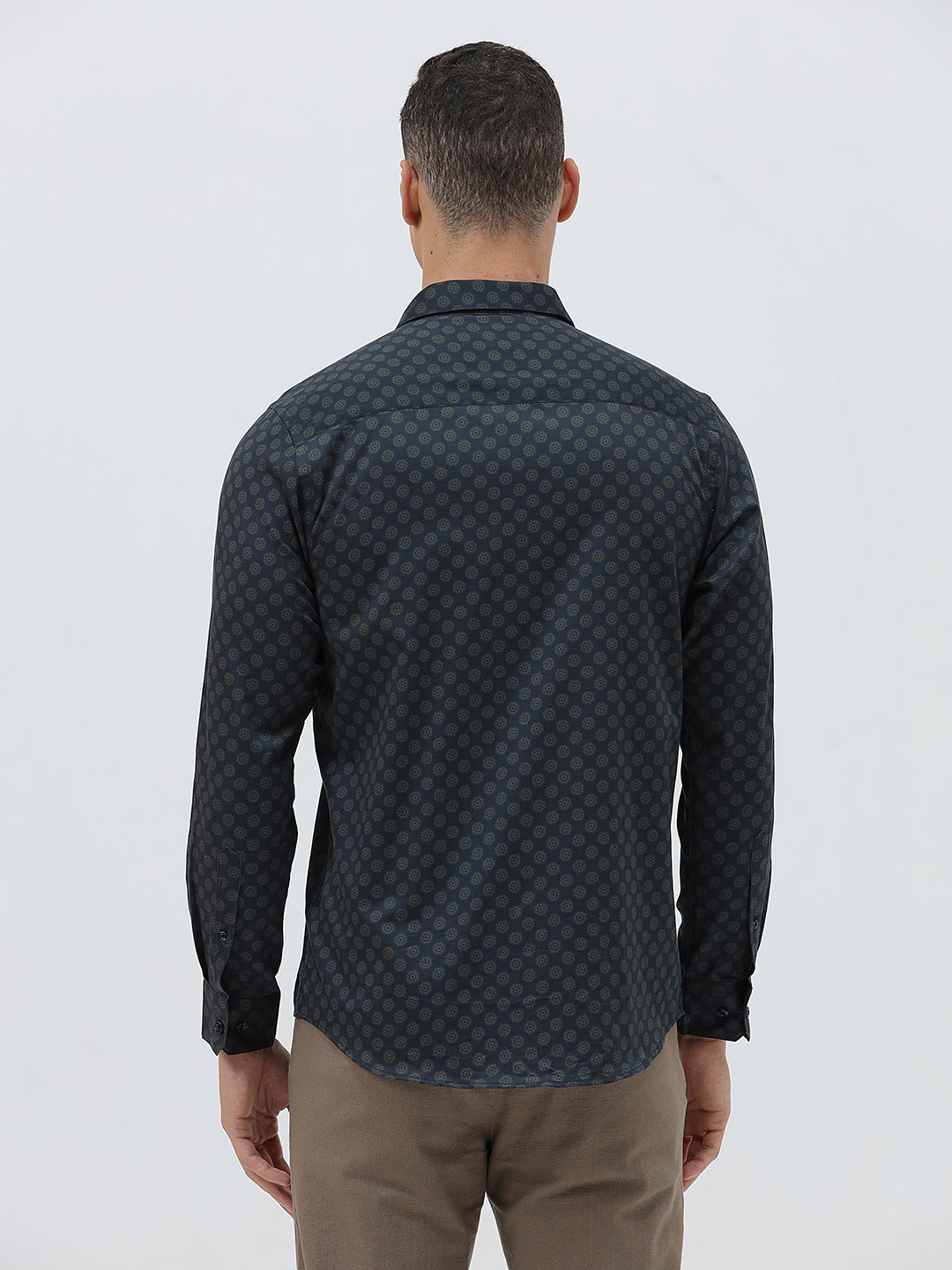A man wearing a dark navy long-sleeve button-up shirt with a small geometric pattern and rolled-up sleeves, paired with khaki pants, against a plain light gray background.