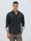 A man wearing a dark navy long-sleeve button-up shirt with a small geometric pattern and rolled-up sleeves, paired with khaki pants, against a plain light gray background.