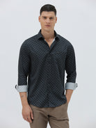 A man wearing a dark navy long-sleeve button-up shirt with a small geometric pattern and rolled-up sleeves, paired with khaki pants, against a plain light gray background.