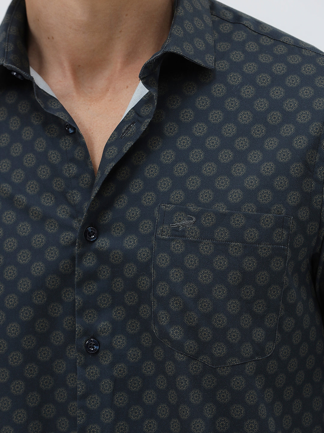 A man wearing a dark navy long-sleeve button-up shirt with a small geometric pattern and rolled-up sleeves, paired with khaki pants, against a plain light gray background.