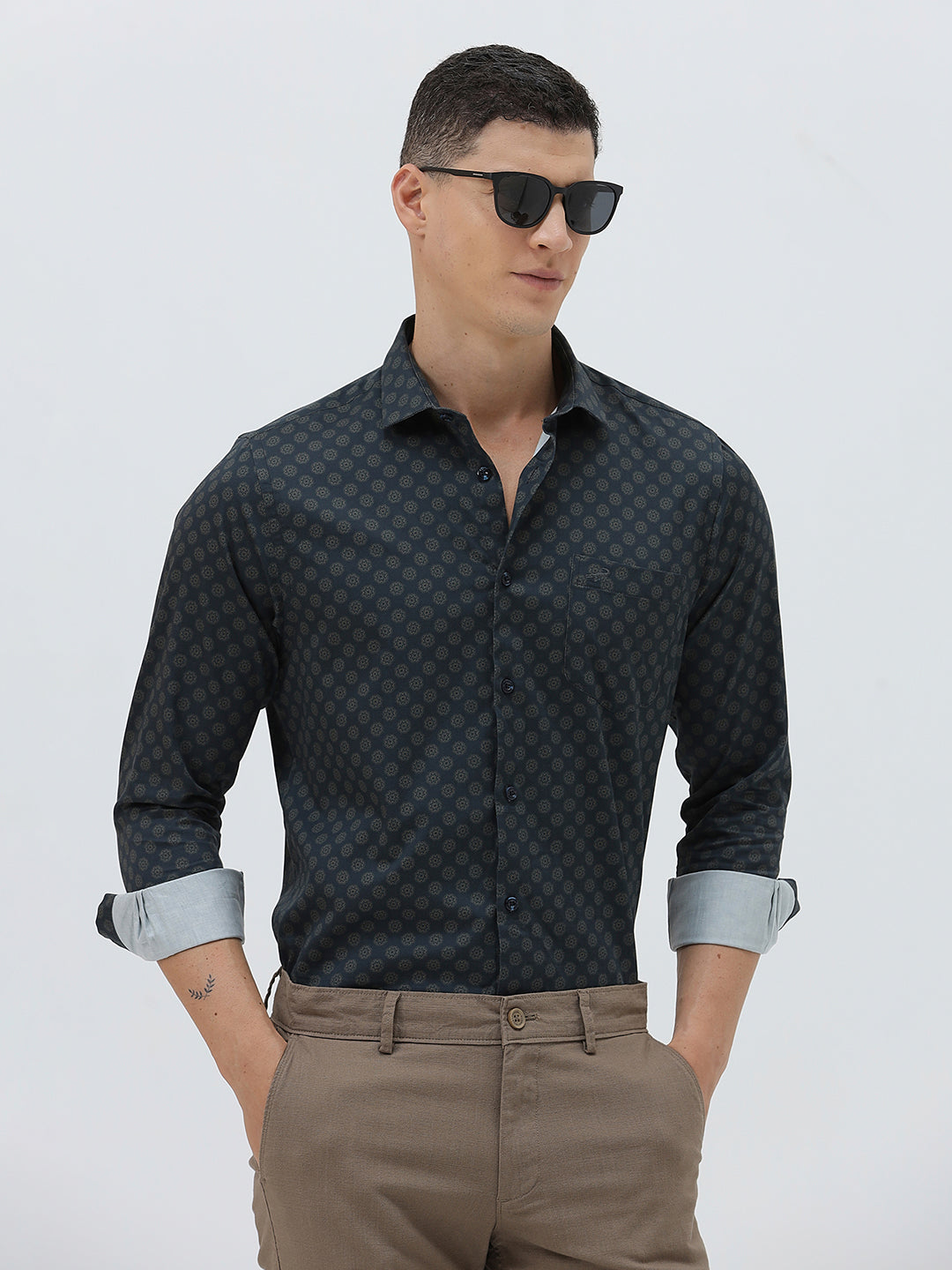 A man wearing a dark navy long-sleeve button-up shirt with a small geometric pattern and rolled-up sleeves, paired with khaki pants, against a plain light gray background.