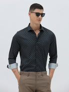A man wearing a dark navy long-sleeve button-up shirt with a small geometric pattern and rolled-up sleeves, paired with khaki pants, against a plain light gray background.